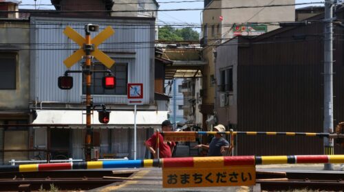 two men are talking aside the San-yo Line as they wait for the passing of an approaching train.
