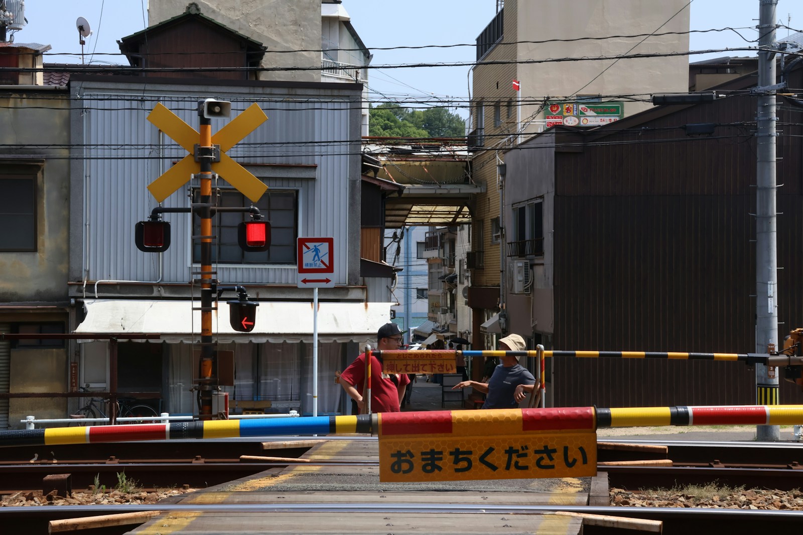 two men are talking aside the San-yo Line as they wait for the passing of an approaching train.